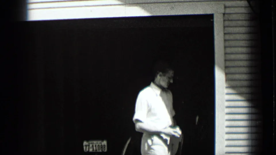 Near the end of the clip, the man turns his head and body to the side while holding the cloth in the doorway setting.