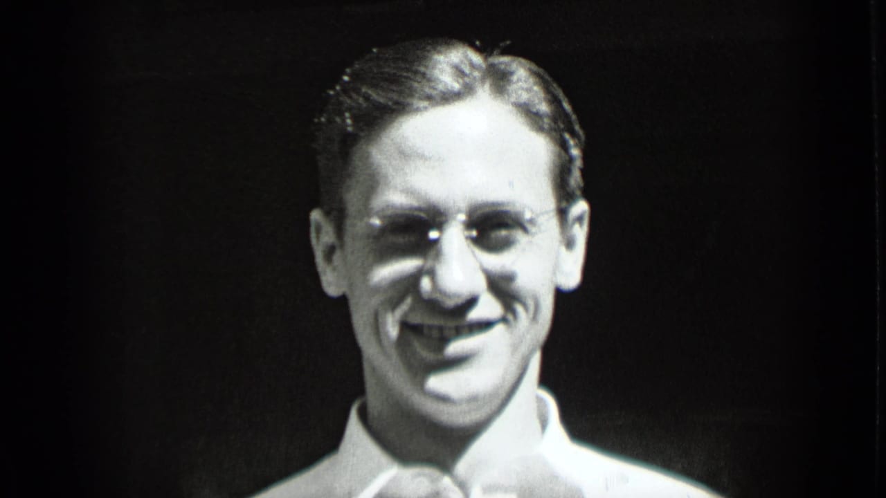 Smiling young man with round glasses and a white collared shirt against a dark background.