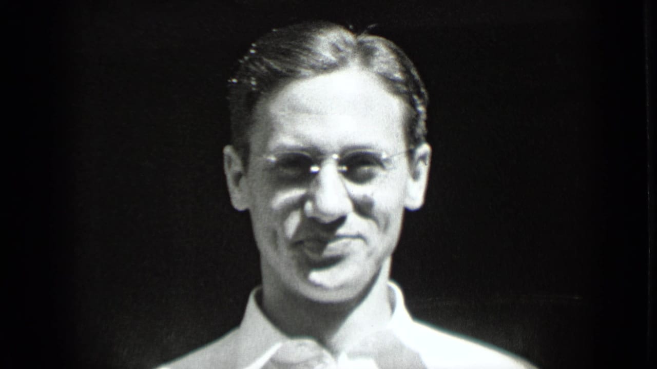 Close-up of a young man wearing eyeglasses and a light shirt against a dark background.