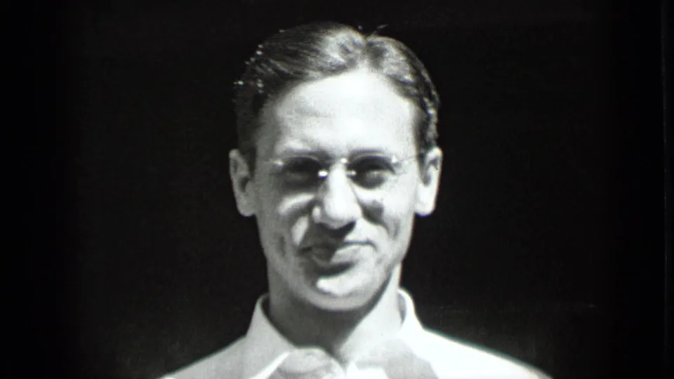 Close-up from 1939 New York home-movie footage showing a young man in eyeglasses and a light dress shirt smiling faintly.