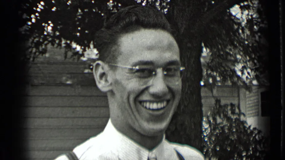 Close-up from the 1939 New York home movie showing the young man laughing or smiling broadly near a tree and house exterior.