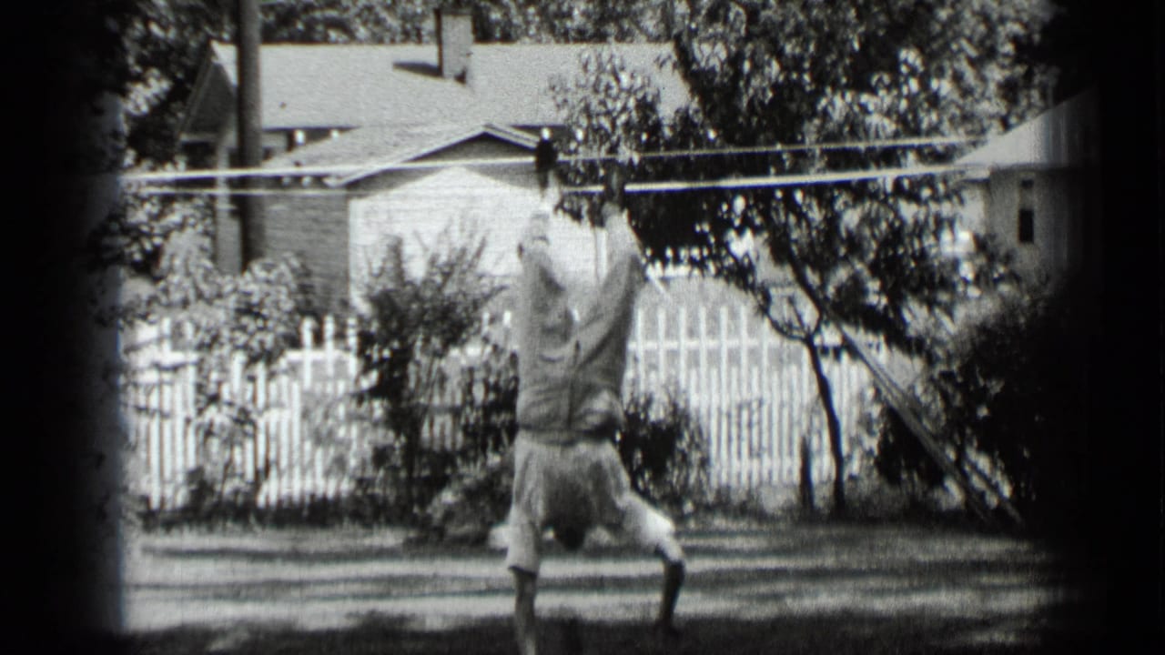 Young man starts a handstand in a New York backyard, with grass, trees, and a picket fence behind him.