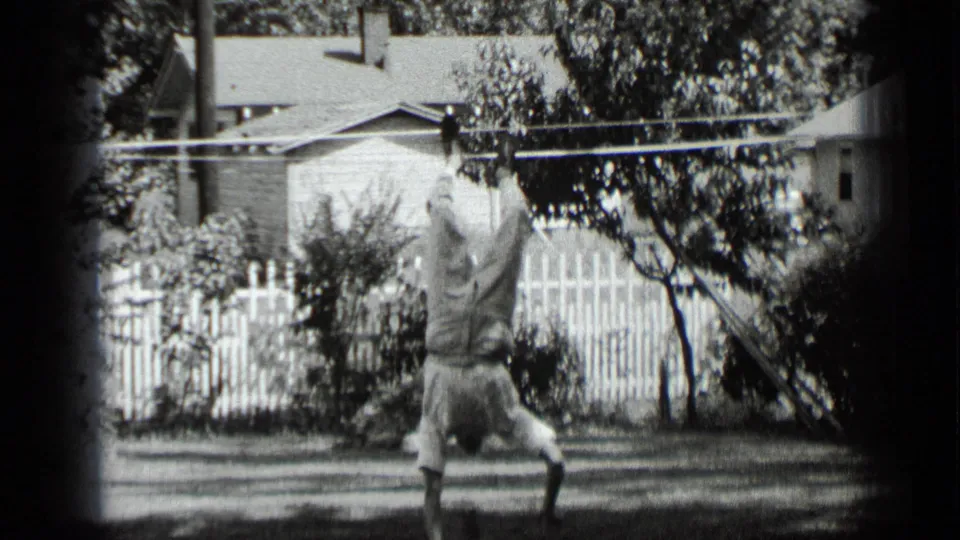 Young man starts a handstand in a New York backyard, with grass, trees, and a picket fence behind him.