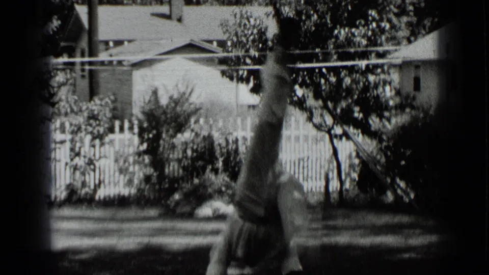 In 1939 New York home-movie footage, a boy balances upside down on grass with a fence, trees, and house behind him.