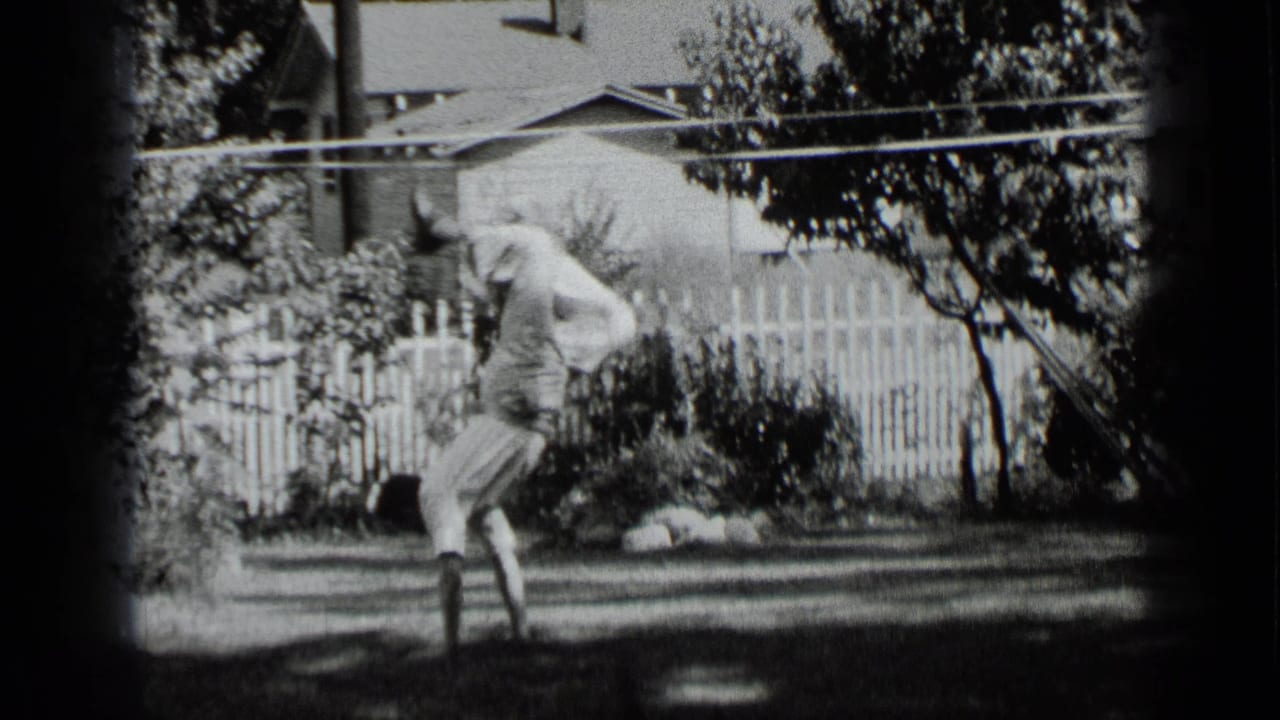 Man in light clothing balances upside down on the grass near a white picket fence.