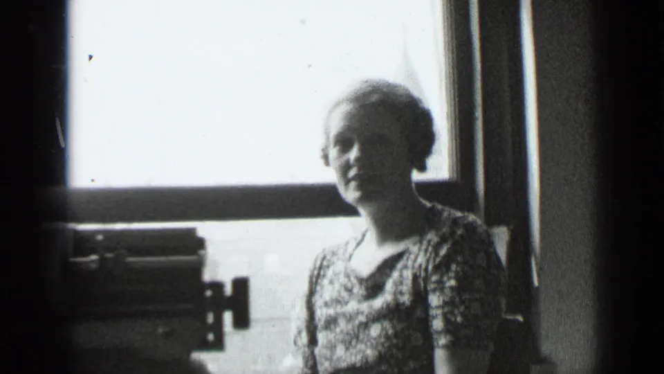 In 1939 New York home-movie footage, a woman stands by a bright window while a typewriter sits in shadow at the lower left.