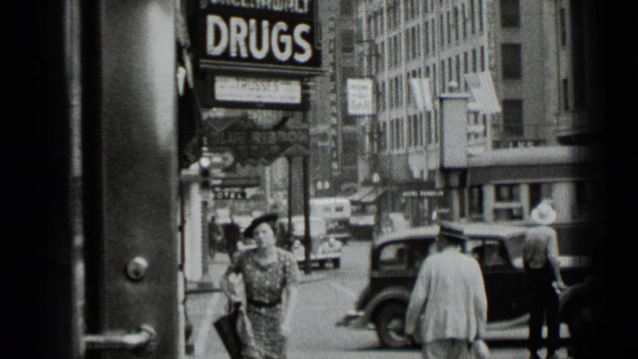 Woman in patterned dress walks on a busy sidewalk near a large DRUGS sign and parked cars.