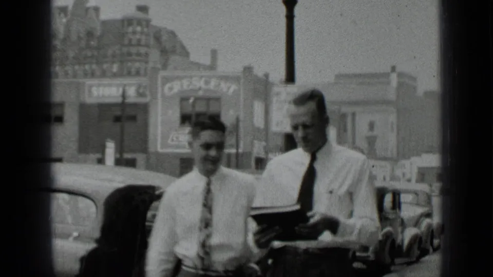 Men in ties pass in front of parked cars, with Crescent Chevrolet signage visible in the 1939 New York street scene.