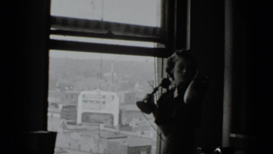 The woman remains near the window with the telephone receiver, partly silhouetted against the exterior cityscape.