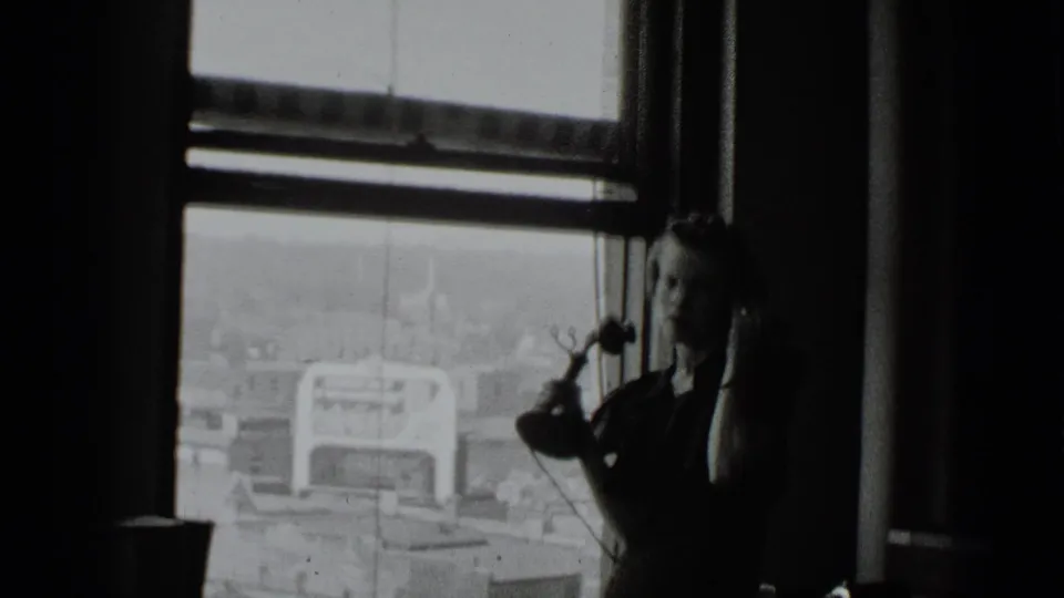 Near the end of the clip, the woman holds the telephone beside the window, with rooftops and a bright exterior sign behind her.