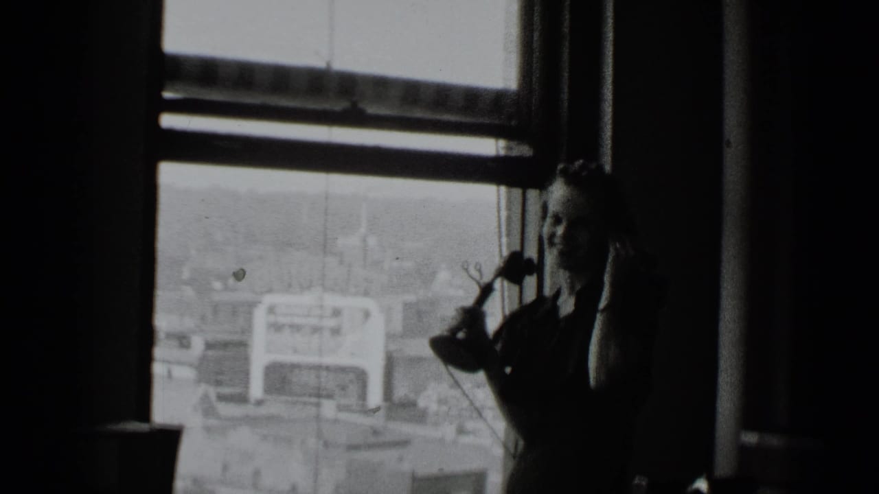 Dim interior with a large window, city view, and a partly visible woman near the frame edge.