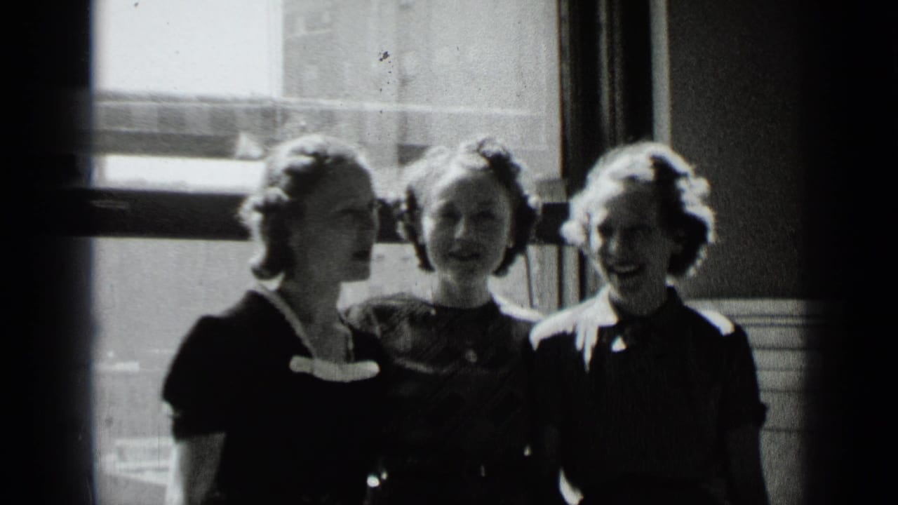 Three young women stand together by a bright window inside a building.