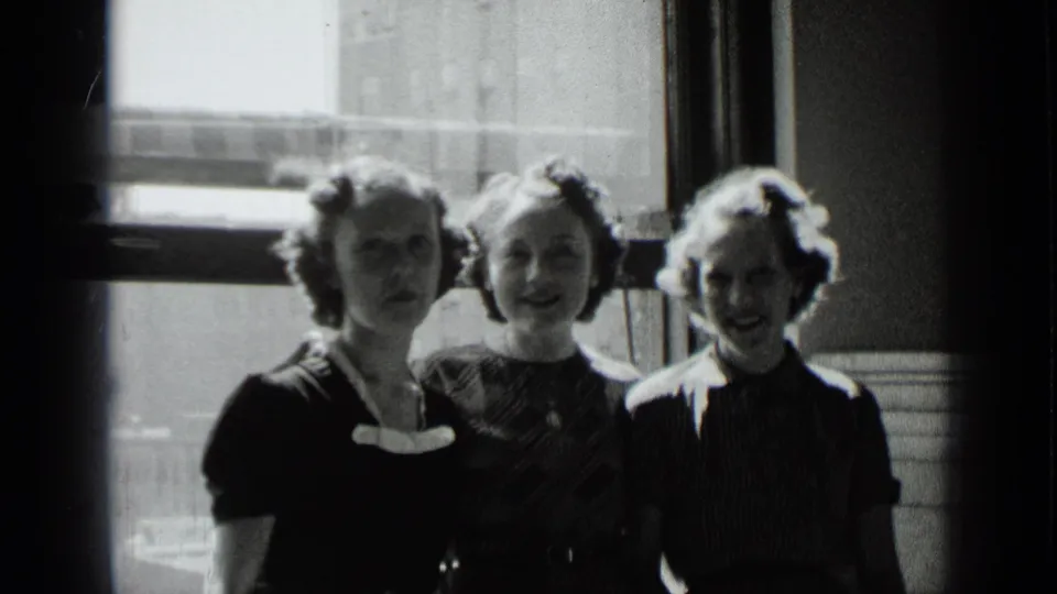 Three young women stand in a row beside a bright window in 1939 New York home-movie footage.