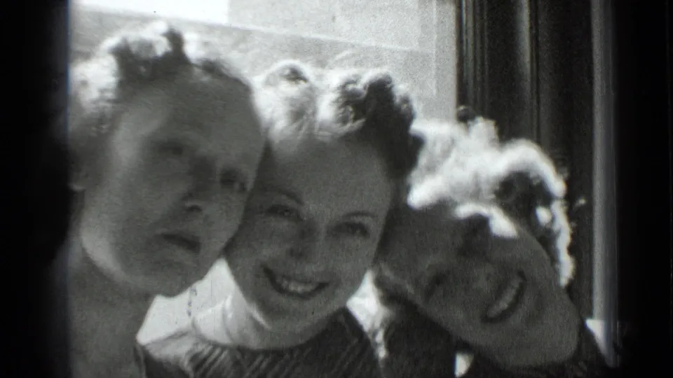 Three women in a 1939 New York interior pose shoulder to shoulder near a window, one leaning playfully toward the group.