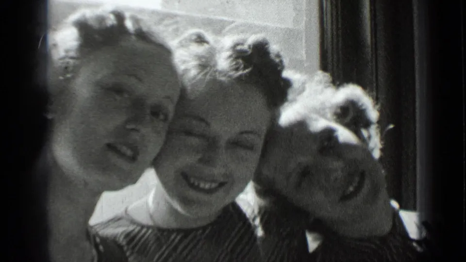Three women in black-and-white 8mm footage lean together near a window, with soft focus and bright backlight.