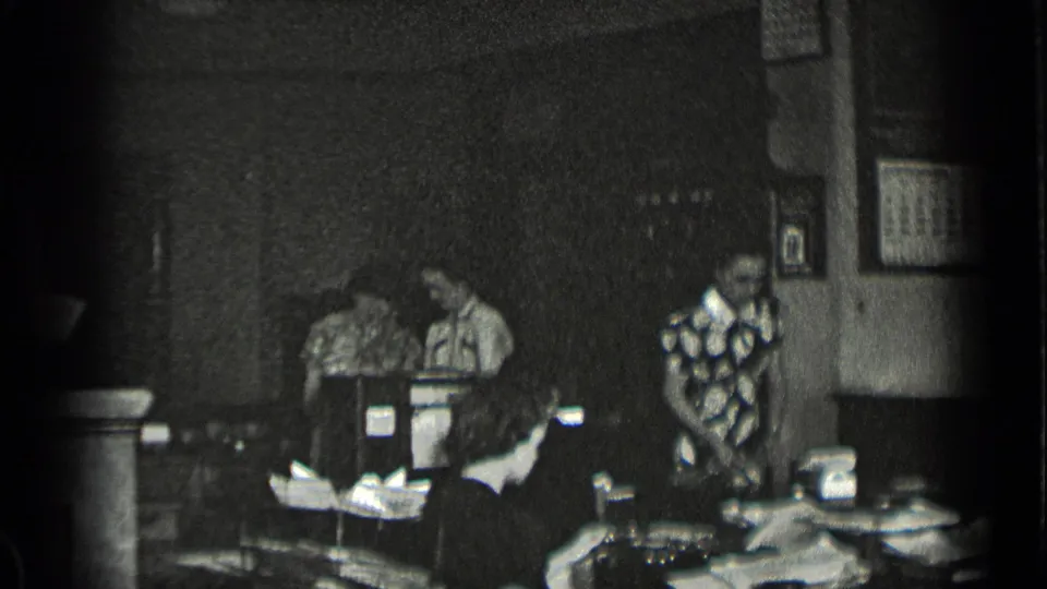 A wider 1939 New York office view shows multiple workers seated at desks with papers and wall frames visible in the background.