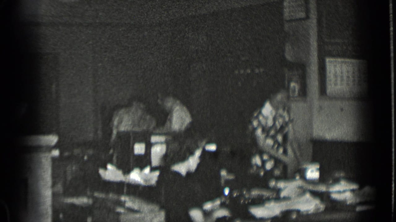 Women working around tables in a dim sewing shop interior.