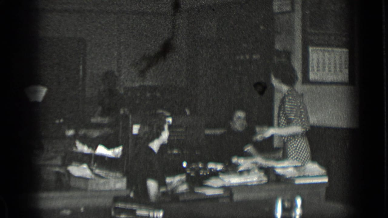 Women working around a cluttered office desk with papers and an office machine.