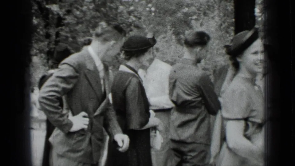 Young adults in formal everyday clothing stand close together in a sunny New York outdoor setting with trees in the background.