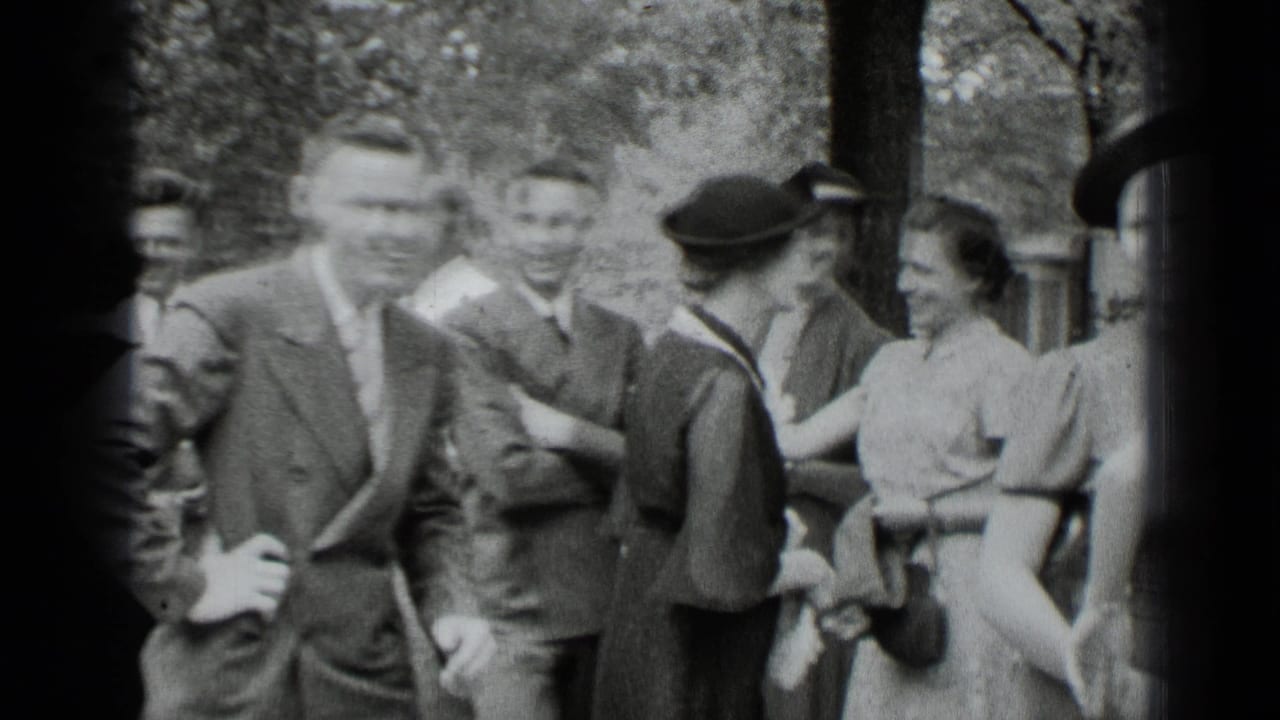 Adults in suits and dresses greet one another in a shaded outdoor park area.