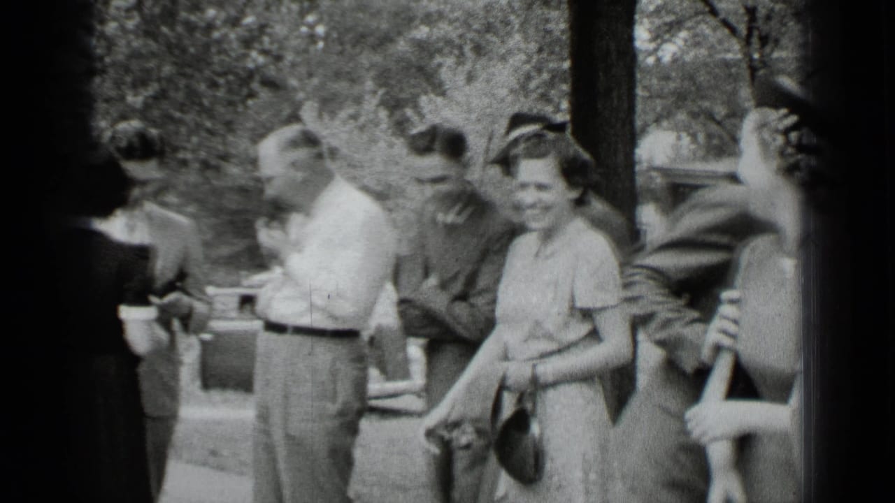 A woman in a light dress smiles toward the camera while men in shirts and jackets gather nearby in New York.