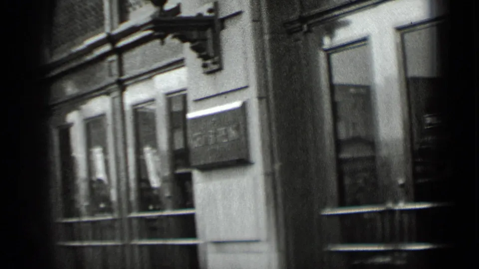 The final frame shows a blurred 1939 New York storefront facade with windows, signage, and handheld framing from the sidewalk.