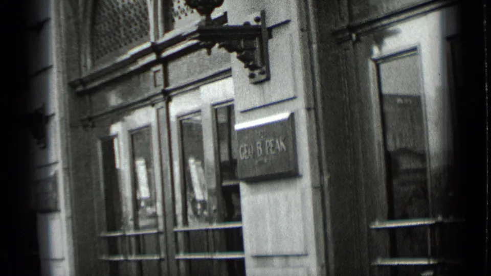 1939 New York 8mm frame showing a masonry building entrance with glass doors, sconces, window grilles, and a visible wall plaque.