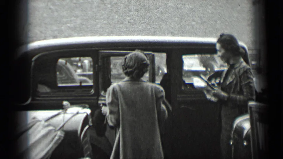 A woman appears to handle the door of a parked car while another woman stands at the curb in 1939 New York footage.