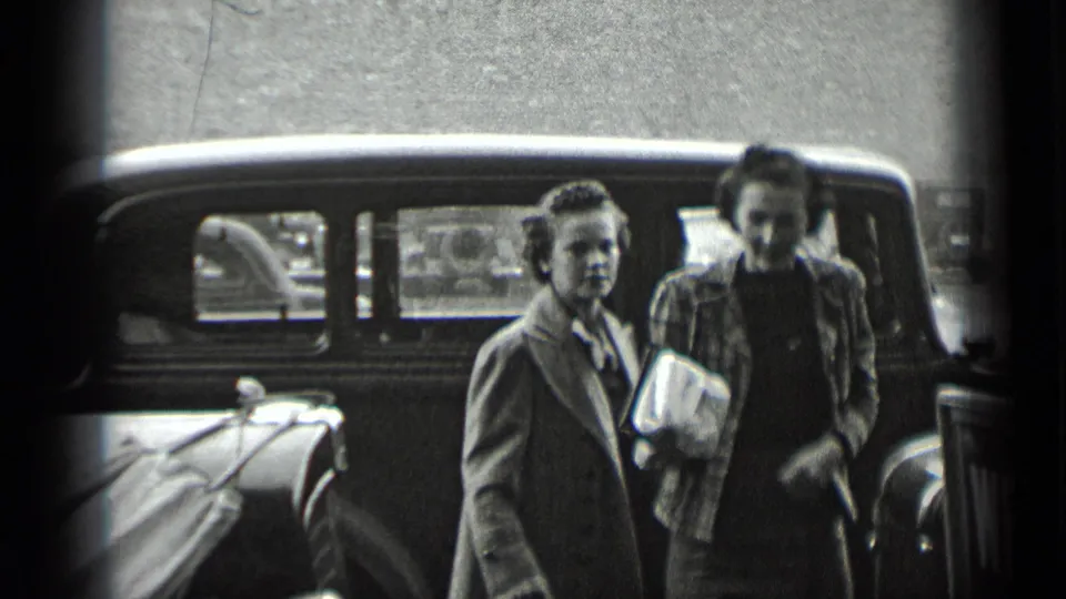 Two women in coats stand by a parked automobile, one holding a light-colored bag, in 1939 New York street footage.