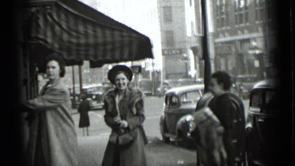 Several women are visible near a storefront awning and parked cars on a New York city street in 1939 home-movie footage.