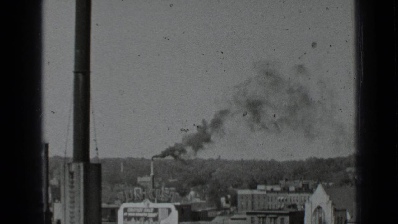 City rooftop view with a chimney releasing dark smoke into the sky.