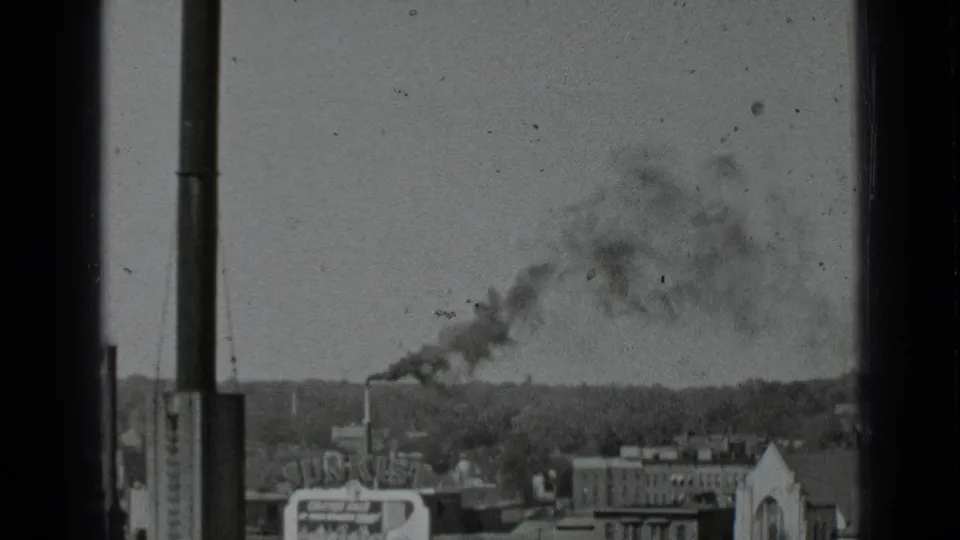 A 1939 New York city view shows rooftops and an industrial chimney sending dark smoke across the skyline.