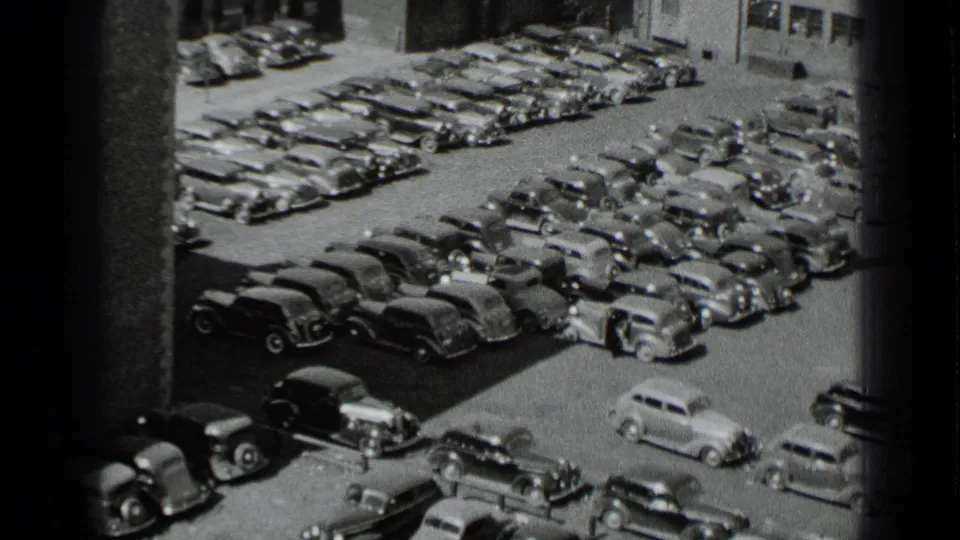 High-angle 1939 New York home-movie frame showing rows of parked cars and a small figure near the vehicles.