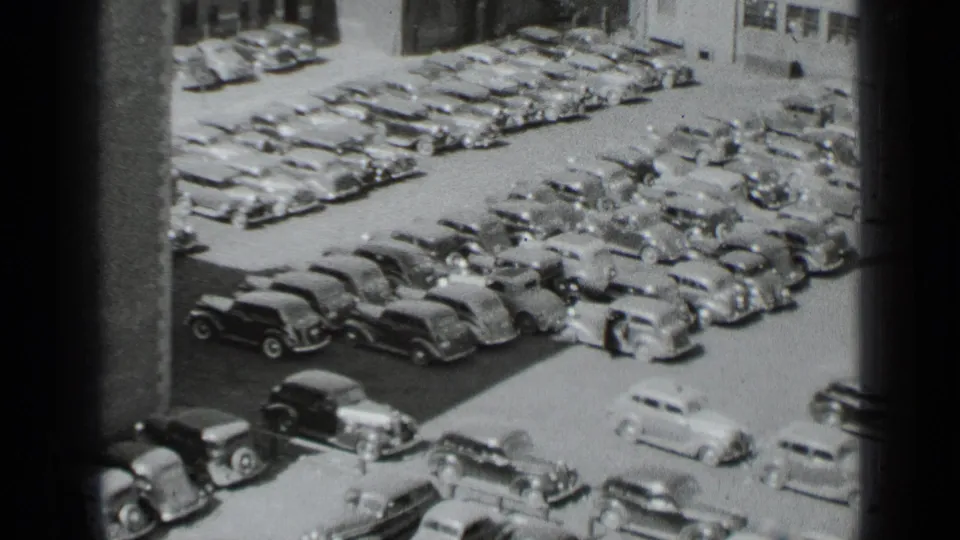 High-angle 1939 New York frame of a light car pulling away amid tightly parked 1930s automobiles.