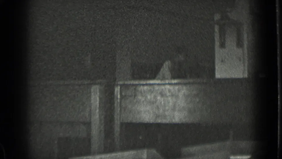 Soft black-and-white 8mm frame with a dark architectural form and heavy grain, location not visually identifiable.