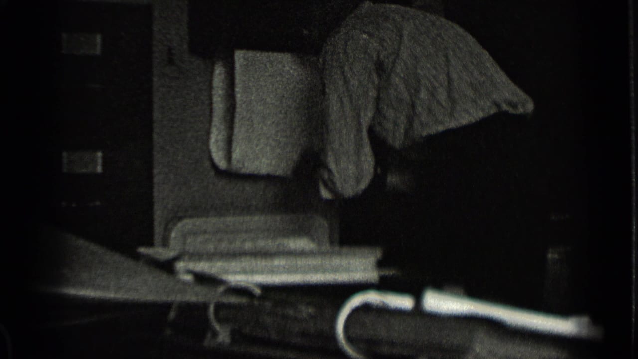 Dark interior or porch view with furniture and a draped cloth in soft black-and-white focus.