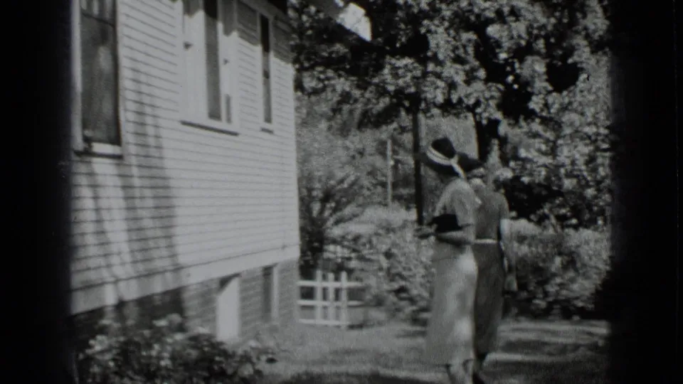 1939 New York home-movie frame showing two women walking away along a garden path beside a clapboard house.