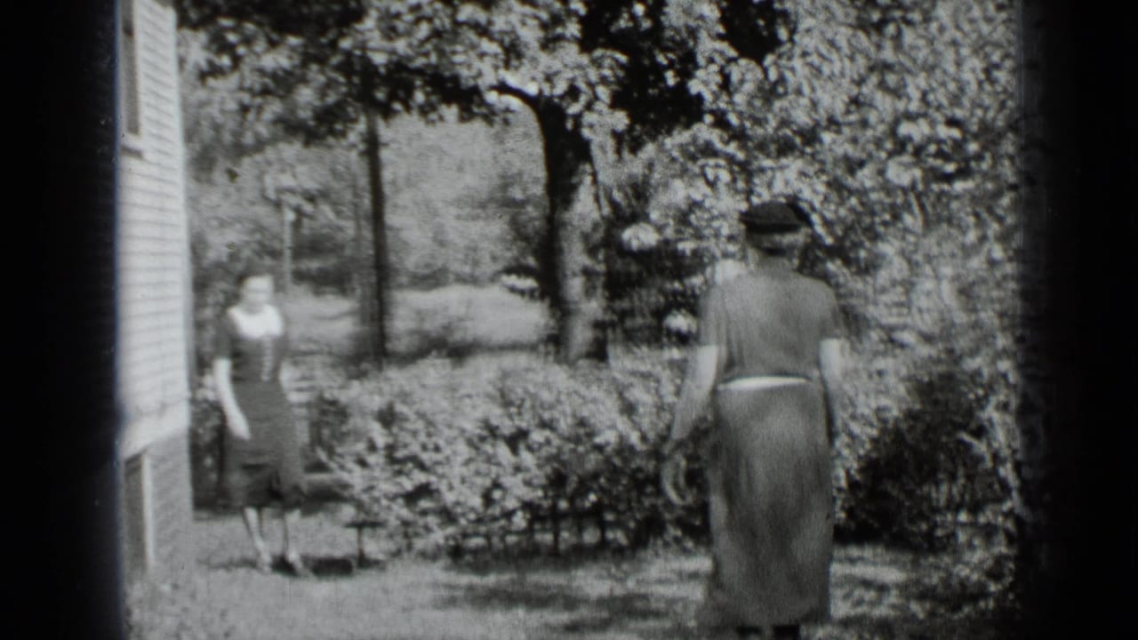 A woman walks across a lawn toward another woman near a house.