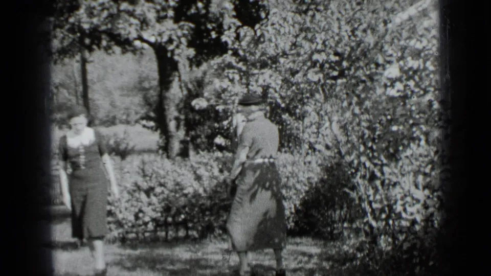 One woman turns or steps across the lawn while another remains near the house in the 1939 New York garden scene.