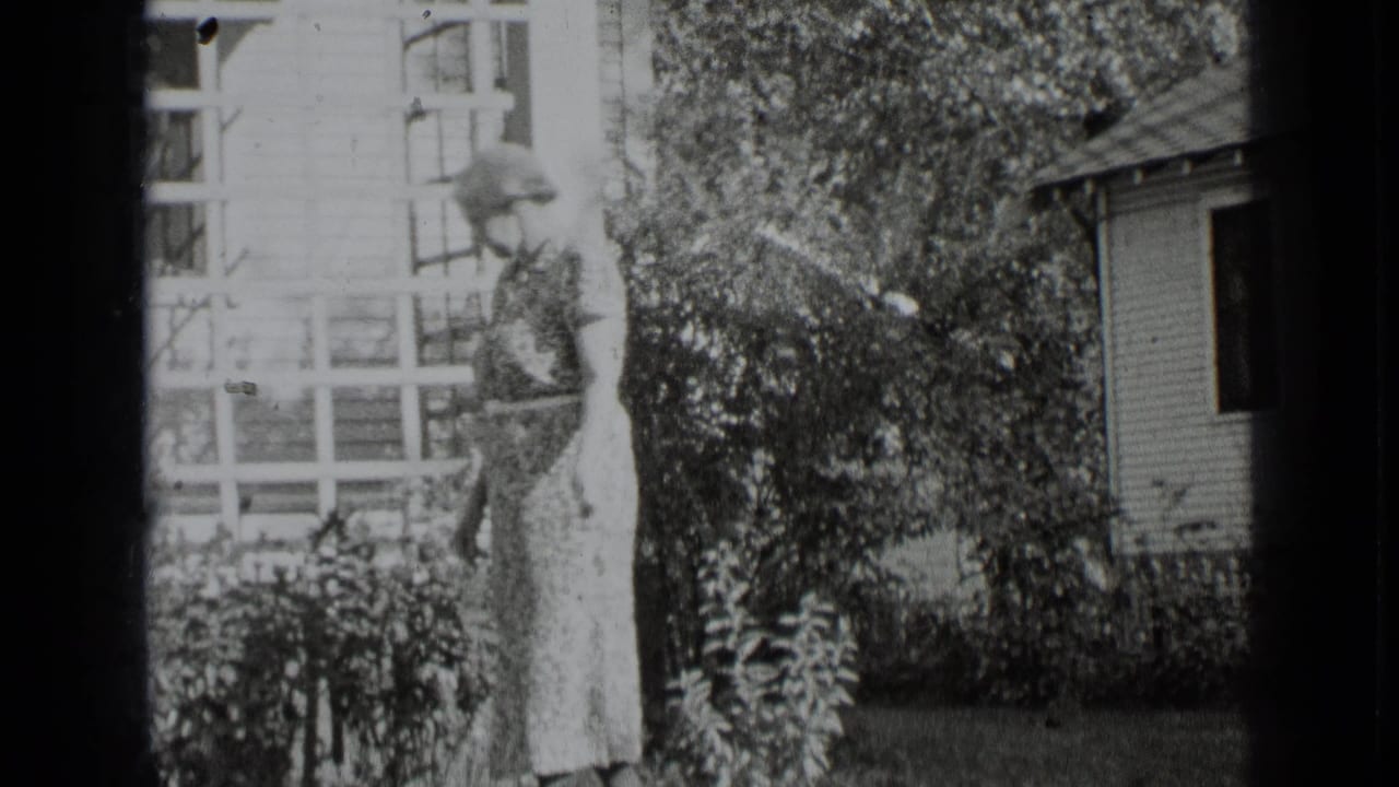 Woman in a long patterned dress walking through a garden beside a house.