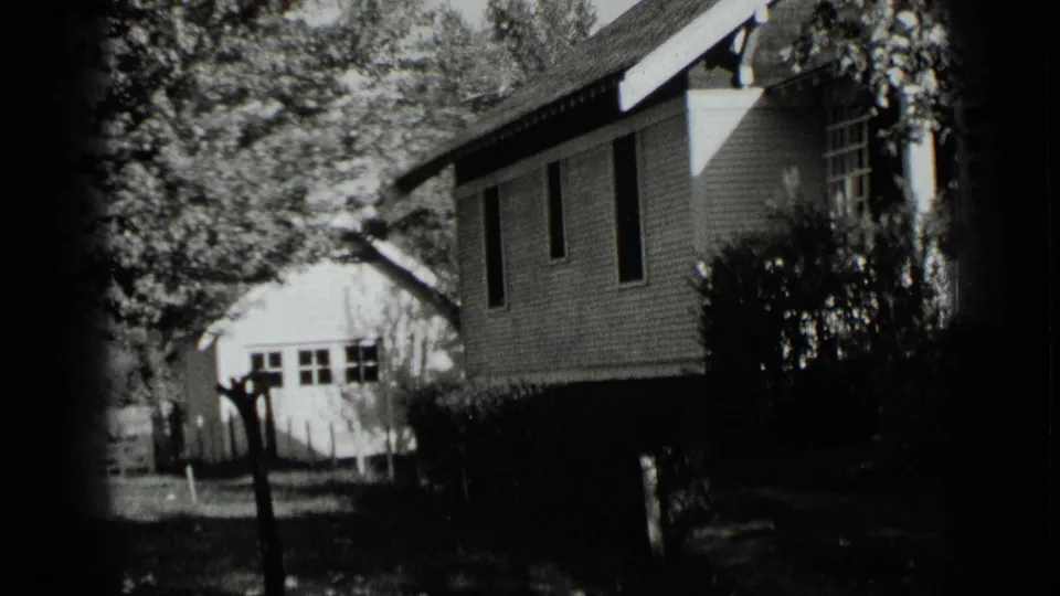A residential exterior in New York, 1939, showing the side of a house, trees, hedges, and a small outbuilding in the yard.