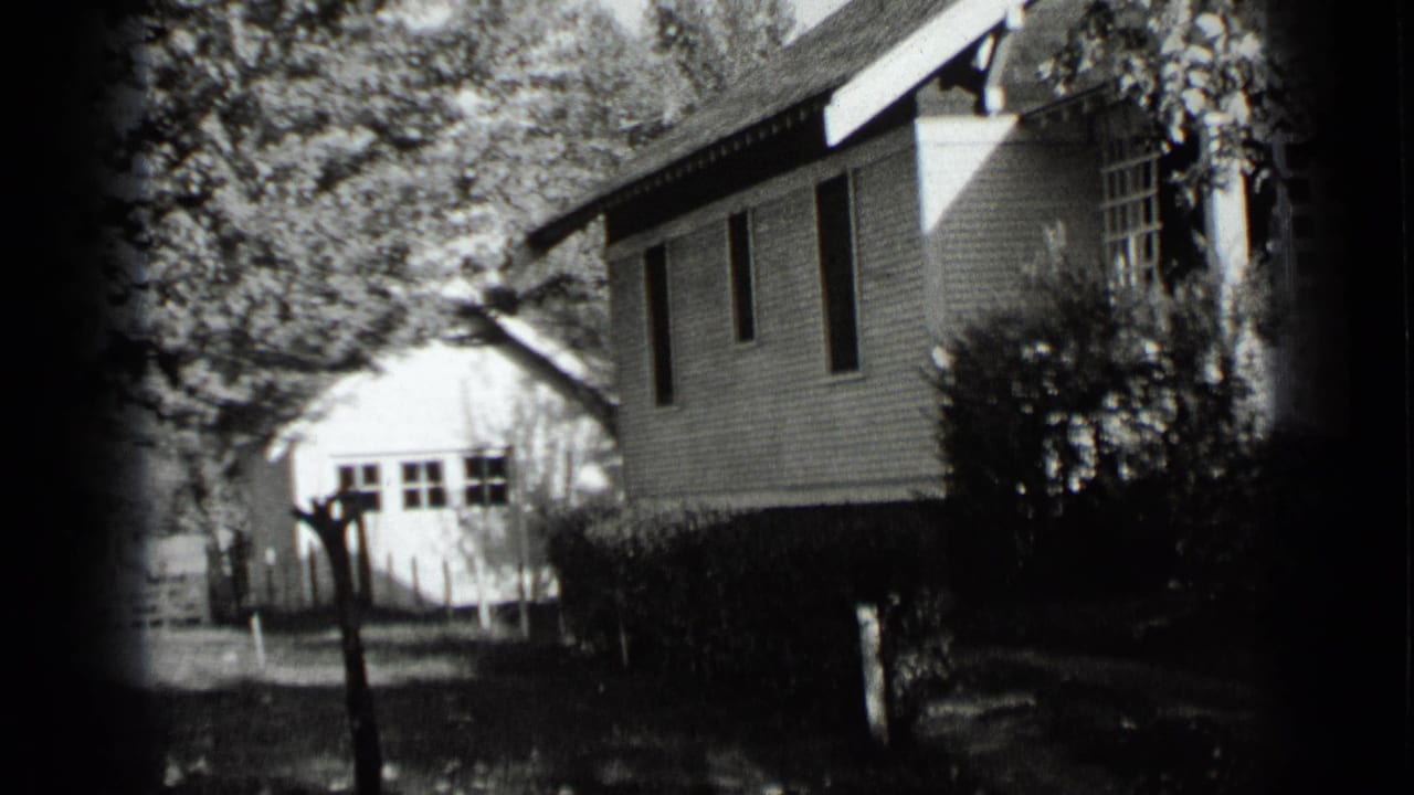 1939 New York 8mm frame showing a white clapboard house, side windows, hedges, trees, and a small outbuilding in the yard.