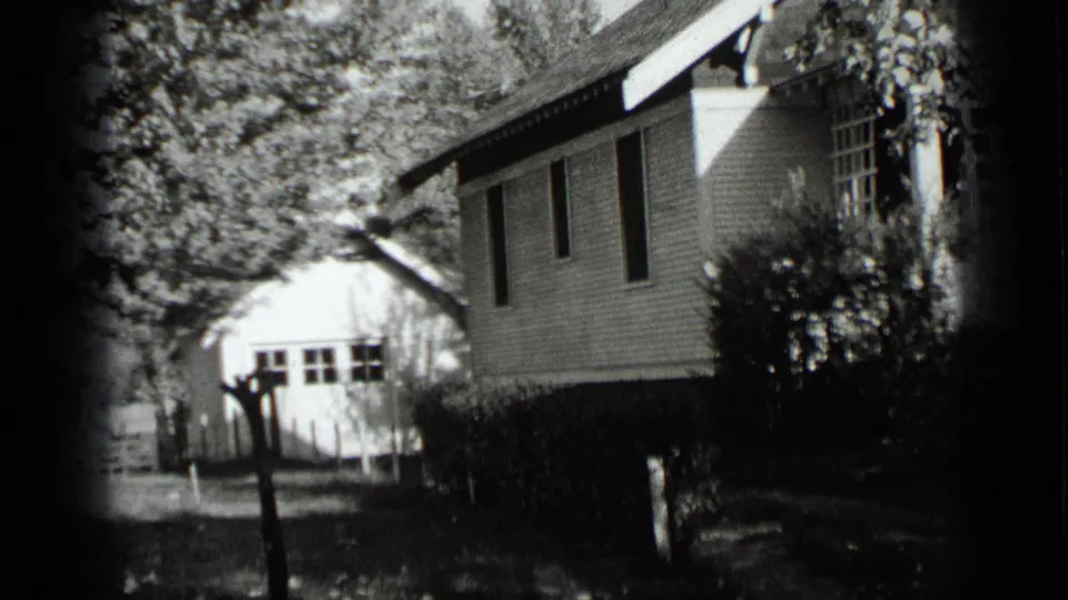 1939 New York 8mm frame showing a white clapboard house, side windows, hedges, trees, and a small outbuilding in the yard.