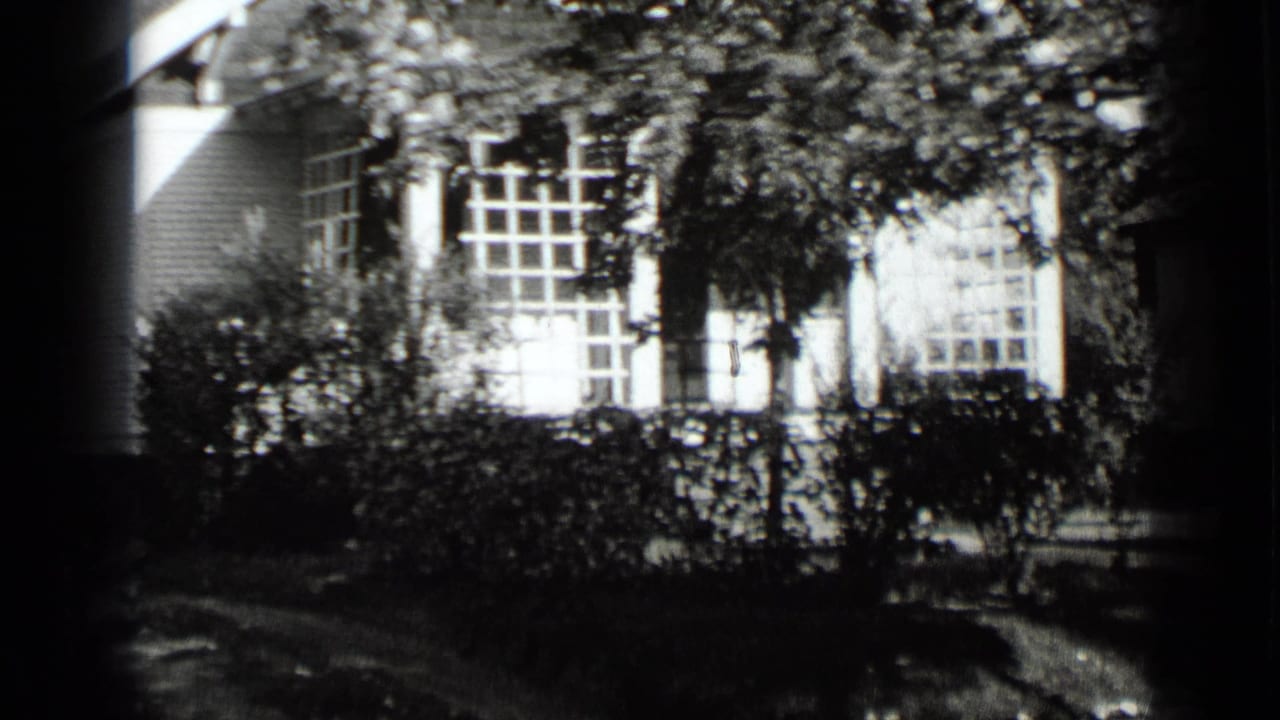 House exterior with multi-pane windows, trees, hedges, and sidewalk shadows.