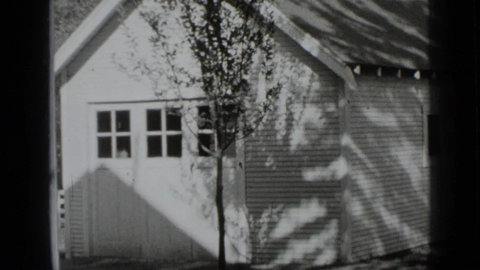 1939 New York home-movie frame showing a small clapboard house, gabled roof, multi-pane windows, and tree shadows.
