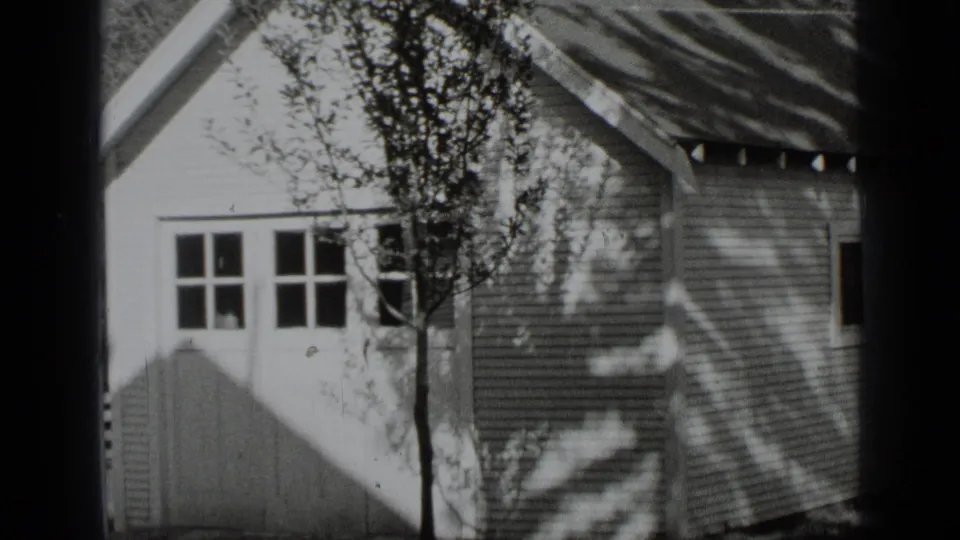 1939 New York residential exterior with multi-pane windows, clapboard siding, roofline, and a tree close to the facade.