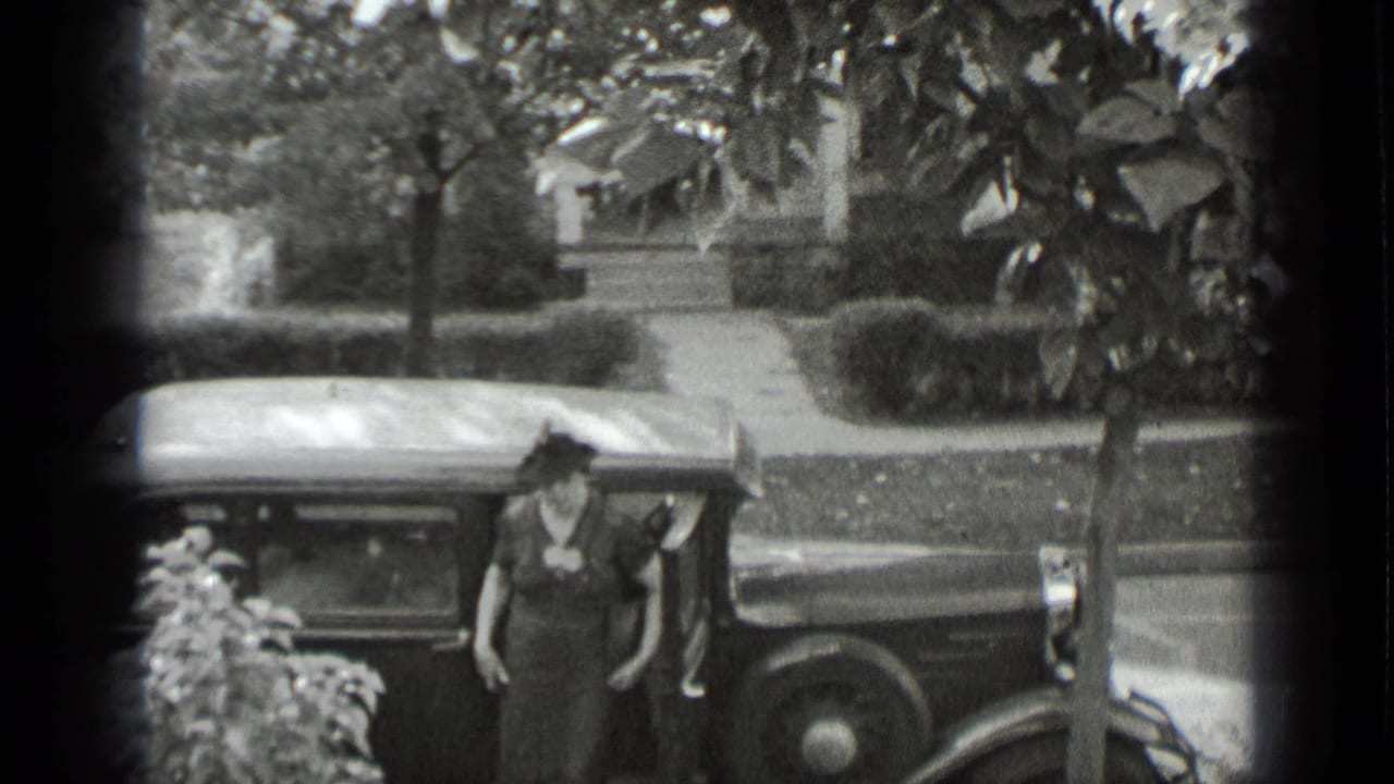 Woman in a dark dress and hat steps away from a vintage car.