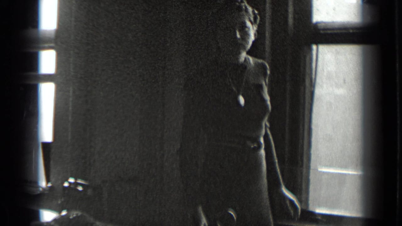 Woman in a dark dress stands near a bright window in a dim interior.