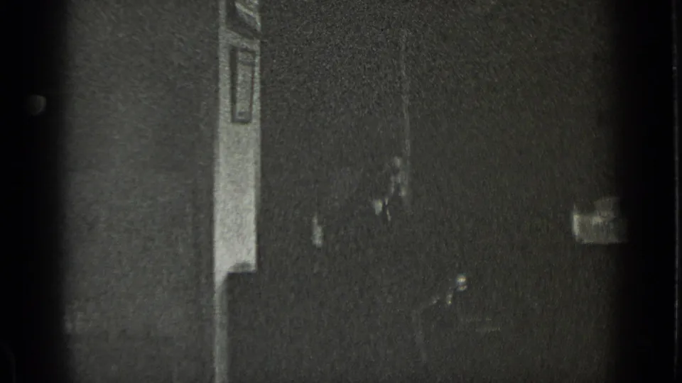 A dim 1939 New York interior shows window light, wall trim, and a partially visible person near the right side of the frame.