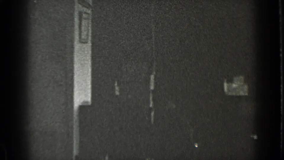 Soft black-and-white 8mm frame from the New York office clip, with a dark interior wall and indistinct doorway or panel detail.